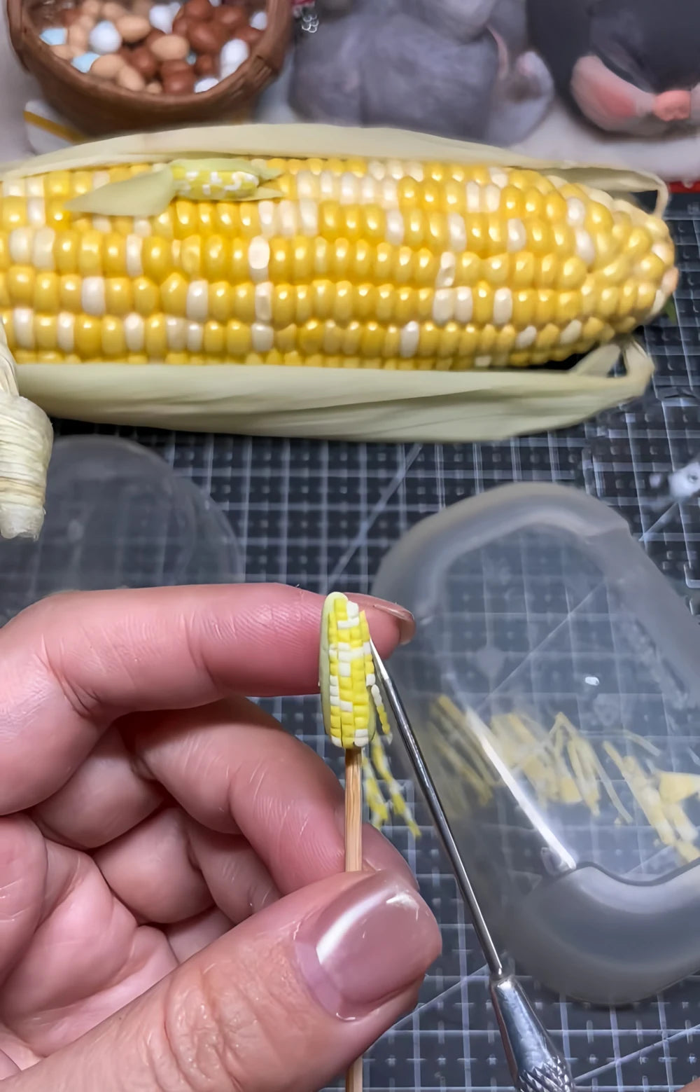 Shaping miniature corn with a sculpting tool beside a full-size corn cob