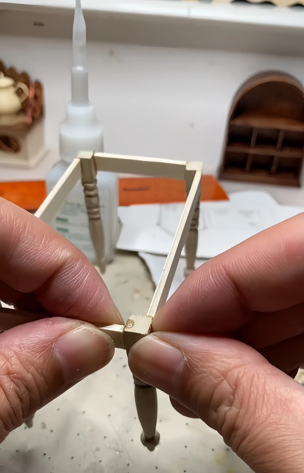 Hands assembling a miniature wooden table frame